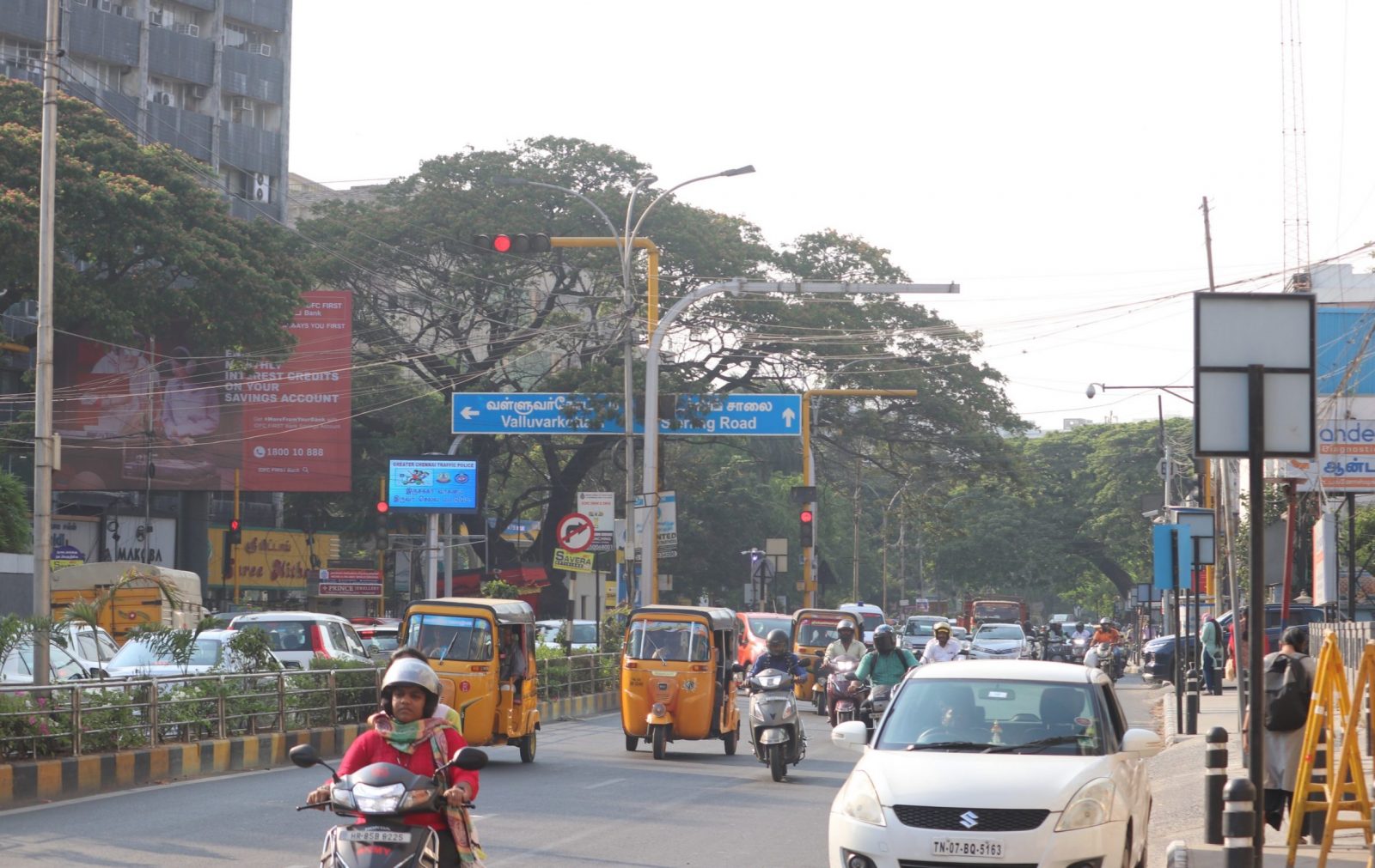 Scene of a bustling road in Chennai with yellow tuk-tuks and trees in the background